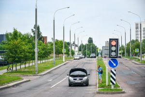 A man stands by his broken car on a city street, looking at his phone.